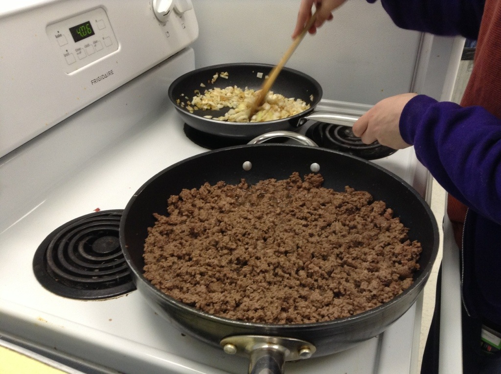 Pan of ground beef+person stirring fried onions and garlic